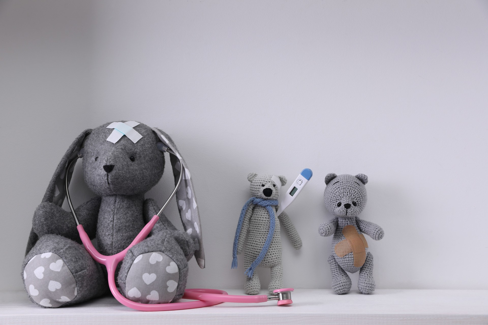 Toys with stethoscope, thermometer and sticking plasters on white table against light grey background. Children's hospital